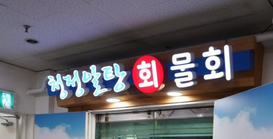 상가 복도 천장 아래 가게 입구 간판 — 하늘색 글씨 «청정알탕», 빨간 원 «회», 흰 글씨 «물회»